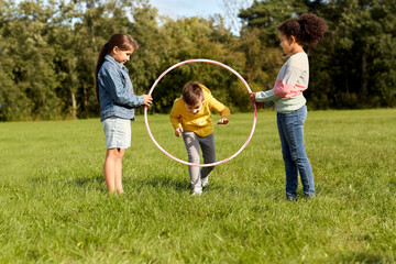 childhood, leisure and people concept - group of happy children jumping through hula hoop at park © Syda Productions