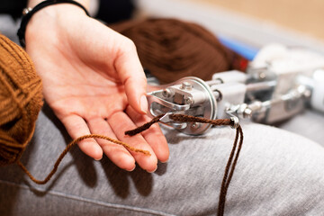 Brown yarn in female hands against the background of a tufted gun.