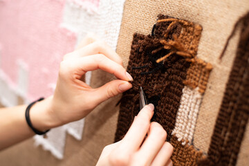 The process of making a tufting rug. Sewing scissors in female hands on the background of a...