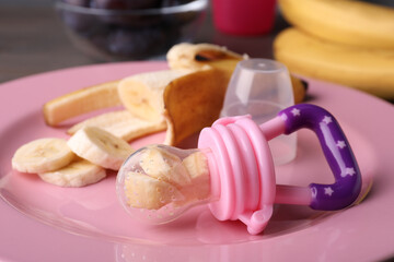 Nibbler with banana and fresh fruit on pink plate, closeup. Baby feeder