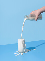 Pouring milk into the glass on a blue background. Spilled milk on the table.