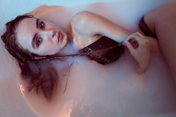 Fototapeta premium Playful brunette posing in a bathtub wearing underwear in the neon light. Dark image