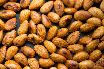 Filled frame background wallpaper shot of a bunch of crunchy roasted almonds with sea salt on a black background