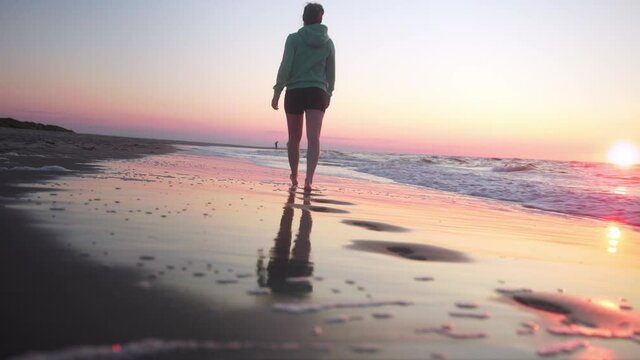 Walking woman on the shore in the sand and waves at sunset, Baltrum Island, North Sea