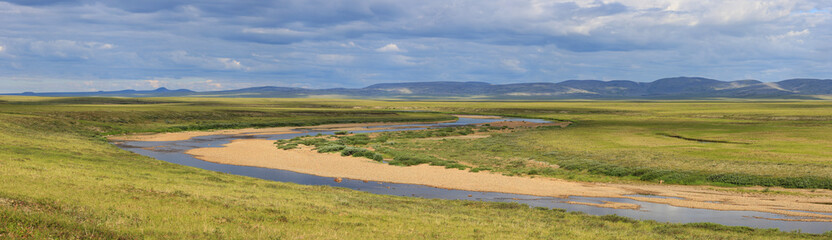 Fototapeta na wymiar Wide panorama of a meandering river in the tundra in the Arctic. Summer season in the tundra. Picturesque northern nature of polar Siberia and Chukotka. Travel and hikes to the extreme North of Russia