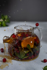 Tea splash with citrus, cranberries and mint in a glass teapot. Splashing tea