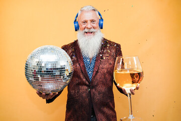 Crazy senior man having fun celebrating new year eve party holding disco ball and glass of wine -...