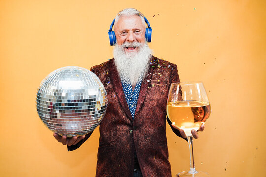 Crazy senior man having fun celebrating new year eve party holding disco ball and glass of wine - Focus on face