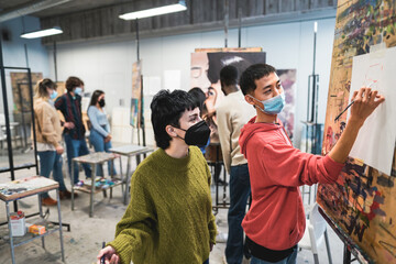 Multiracial students painting inside art room class wearing safety masks - School and healthcare concept - Focus on man face