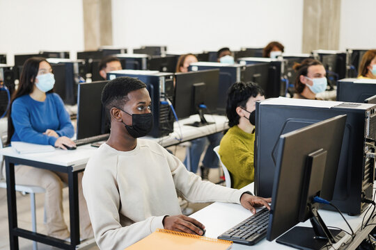 Multiracial Young Students Using Computers Inside Class Room Wearing Safety Masks During Coronavirus Outbreak - Focus African Boy Face