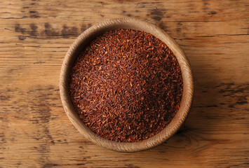 Dry rooibos leaves in bowl on wooden table, top view