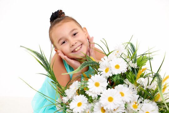 Girl in summer dress in the studio with white background during photo shoot with white flowers daisies