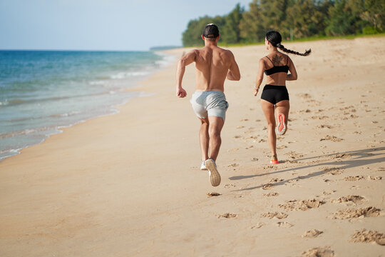 Healthy lifestyle. Jogging outdoors. Young man and woman is running on the sand beach.