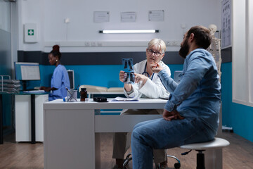 Physician showing x ray scan results to patient at checkup visit, explaining diagnosis and disease. Woman doctor analyzing radiography with man, giving medical addvice and support.