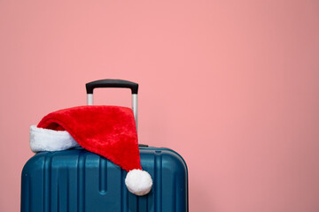 Blue plastic suitcase with Santa Claus hat over yellow background. Concept of travel and visit relatives on Christmas Holidays