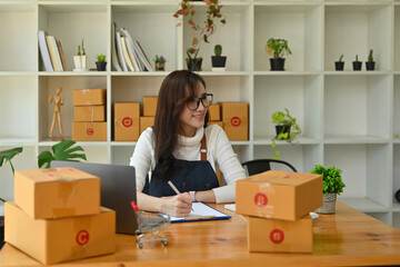 Photo of a beautiful woman writing the address on a cardboard box while sitting in front of her...