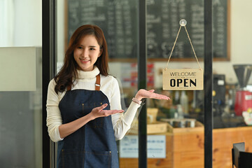 Photo of young restaurant owner while standing in front of the restaurant glass door.