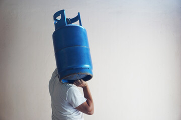 A  man carries blue LPG gas cylinder tank on his shoulder to make delivery to local customers in...