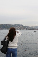 a girl in a white sweater feeds seagulls by the sea