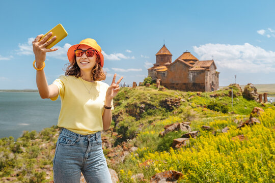 Happy woman tourist taking selfie photo at the background of famous Armenian Hayravank Monastery. Travel blogger concept