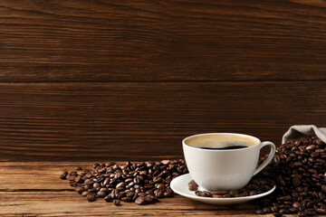 Cup of aromatic hot coffee and beans on wooden table, space for text