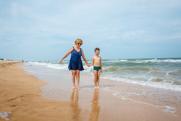 A grandmother is playing with her grandson on the beach when the wave crashes on their feet.