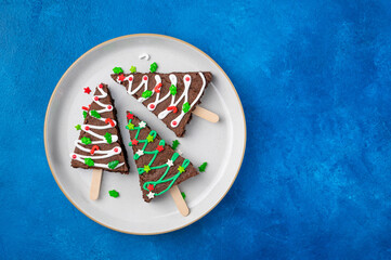 Christmas chocolate brownies with sugar glaze and sprinkles on a blue concrete background....