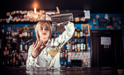Charismatic girl barman formulates a cocktail while standing near the bar counter in pub
