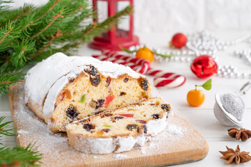 Christmas stollen with dried fruits and powdered sugar on a board on a white wooden background. Copy space.