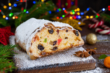 Christmas stollen with dried fruits and powdered sugar on a board on a dark wooden background. Copy space.