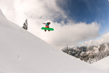 snowboarder performs masterful jump in the air over snowy mountain slope
