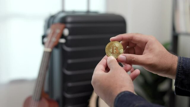 Close up traveler hand man showing cryptocurrency digital coin for travel payment. Trolley bag on the background. New normal pay purchase by digital coin for tourist.
