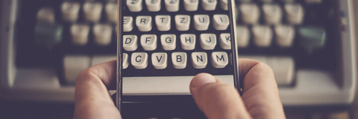 Close up of hands texting and writing on an old typewriter keyboard on modern mobile phone. Concept...