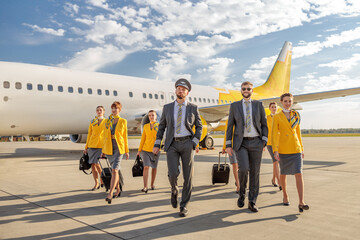 Pilots and stewardesses walking down airfield under cloudy sky