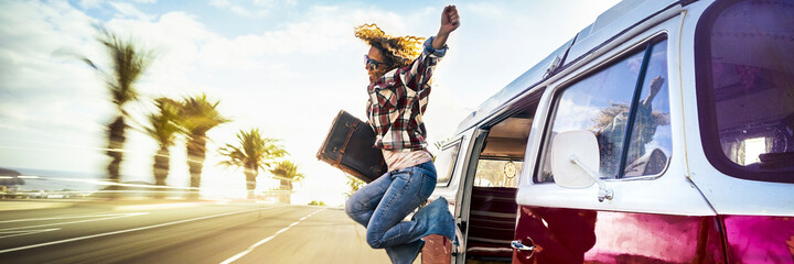 Travel banner header concept with overjoyed adult woman jumping outside a classic van during movement. People have fun in summer holiday vacation trip