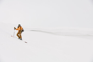 Naklejka na ściany i meble man skier in yellow suit stands and looks to the side against background of white snow