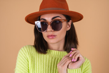 Fashionable stylish woman on a beige background in a sweater and a hat and sunglasses with brown glasses posing