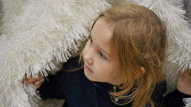 portrait. slow motion Cute preschool girl playing hide and seek in Christmas tinsel. Completely hides in tinsel and exits. Store of New Year's decor and gifts for Christmas