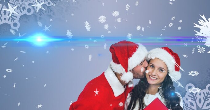 Composition of man kissing happy girlfriend during christmas against glowing background, copy space