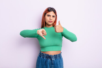 young hispanic woman feeling confused, clueless and unsure, weighting the good and bad in different...