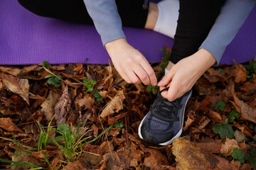 Women's hands are tying the laces of sneakers on a purple rug. Sports in the autumn park