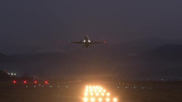 Static view Batumi airport runway at night with commercial airplane departure and caucasus mountains background. Night travel concept aircraft takes-off from ground
