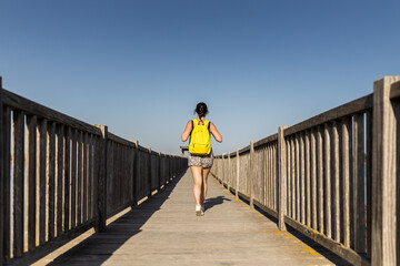 young woman traveler with yellow backpack on a pier on her way to her next trip
