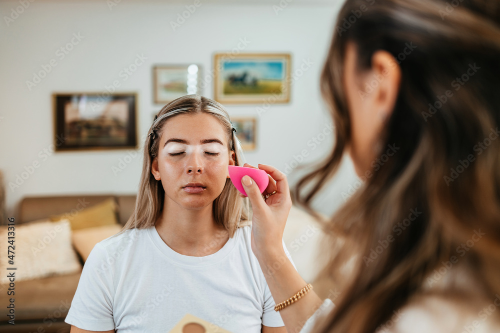 Wall mural Makeup process. Professional artist applying make up on model face. Close up portrait of beautiful blonde woman in beauty saloon.