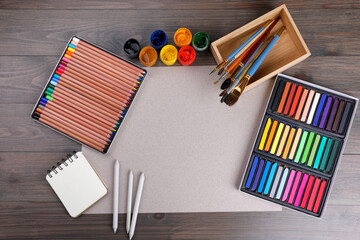 Blank sheet of paper, colorful chalk pastels and other drawing tools on wooden table, flat lay....