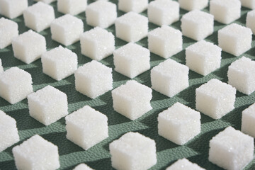 Refined sugar on green background.Cubes of sweet and white sugar in geometricshape. Hard shadows.