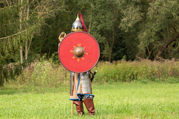 Knight soldier in armour holding red wooden shield during medieval re-enactment in front of green background