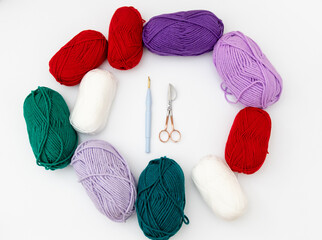 Rounded scissors, punch needle, and skeins of yarn in different colors: white, red, green and purple on white background