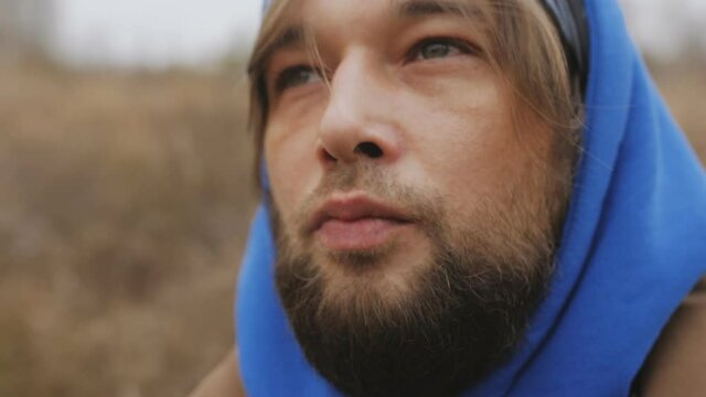 A sad lonely hipster man in an autumn park is sad and looks at the gloomy sky.