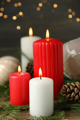 Burning candles and festive decor on wooden table against blurred Christmas lights